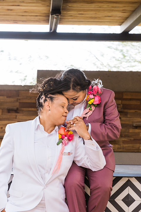  bright and bold lesbian wedding in Palm Springs with one bride in a rose pink suit and the other in a white suit – sitting at the venue 