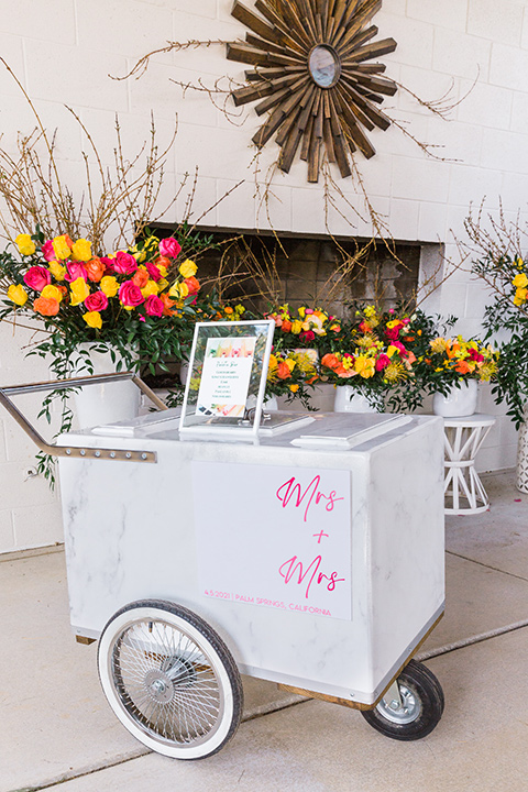  bright and bold lesbian wedding in Palm Springs with one bride in a rose pink suit and the other in a white suit – popsicle cart 