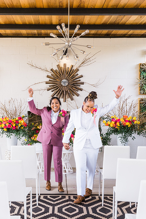  bright and bold lesbian wedding in Palm Springs with one bride in a rose pink suit and the other in a white suit – walk down the aisle 