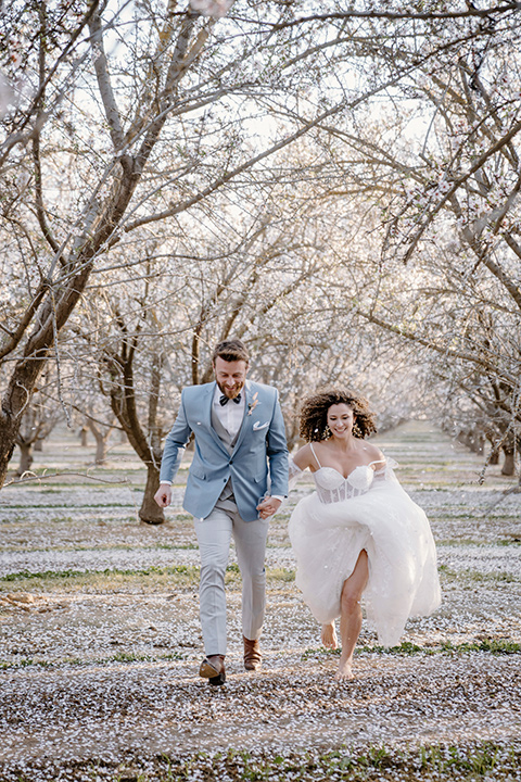  celestial cherry blossom wedding with the groom in a light blue coat and grey pants – couple running