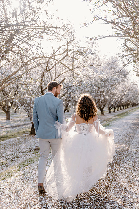  celestial cherry blossom wedding with the groom in a light blue coat and grey pants – couple running 