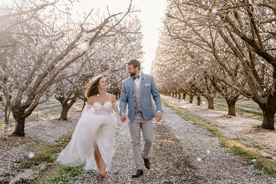  celestial cherry blossom wedding with the groom in a light blue coat and grey pants –couple running