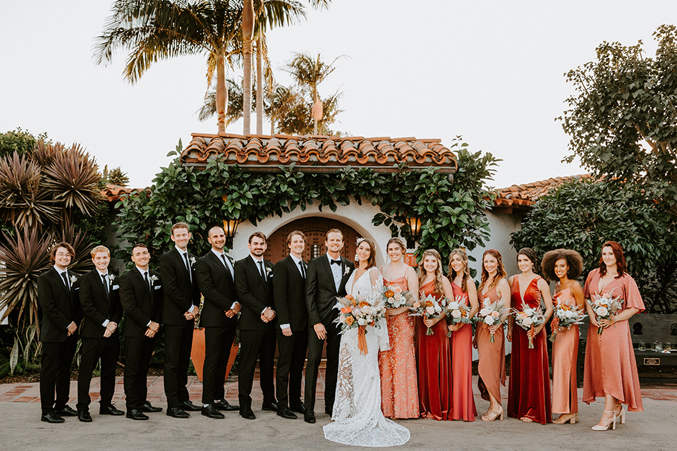  boho beach wedding with Spanish inspired architecture with the bride in a lace gown and the groom in a black tuxedo – group photo