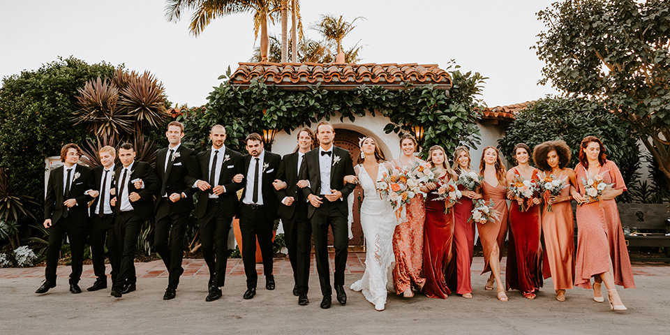  boho beach wedding with Spanish inspired architecture with the bride in a lace gown and the groom in a black tuxedo – group photo