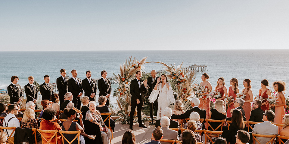  boho beach wedding with Spanish inspired architecture with the bride in a lace gown and the groom in a black tuxedo – ceremony photo