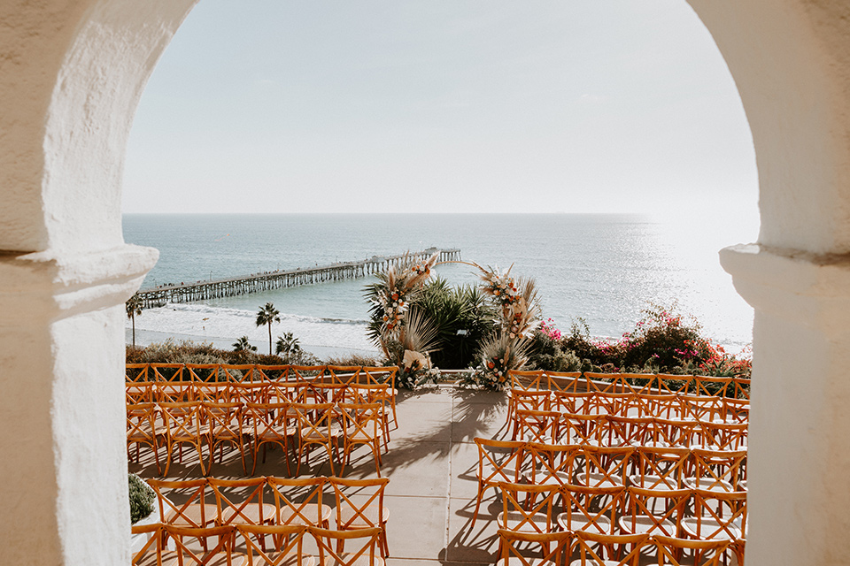  boho beach wedding with Spanish inspired architecture with the bride in a lace gown and the groom in a black tuxedo – ceremony décor and venue architecture