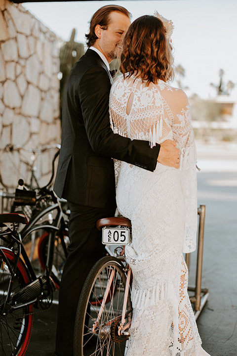  boho beach wedding with Spanish inspired architecture with the bride in a lace gown and the groom in a black tuxedo – couple by the bikes