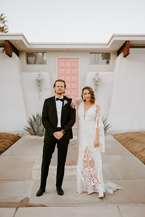  boho beach wedding with Spanish inspired architecture with the bride in a lace gown and the groom in a black tuxedo – couple by pink door