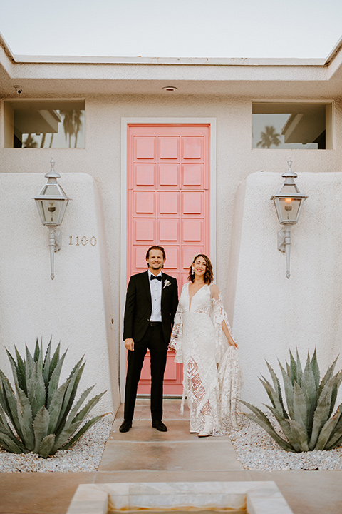 boho beach wedding with Spanish inspired architecture with the bride in a lace gown and the groom in a black tuxedo – couple by pink door 