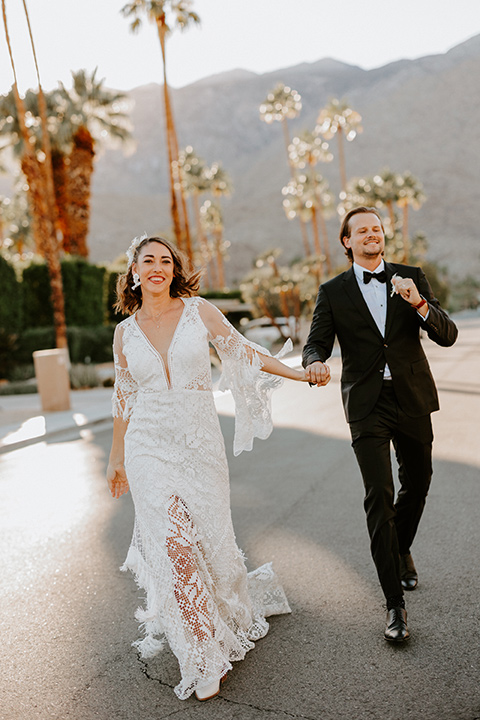  boho beach wedding with Spanish inspired architecture with the bride in a lace gown and the groom in a black tuxedo – couple walking outside 