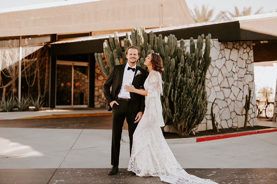  boho beach wedding with Spanish inspired architecture with the bride in a lace gown and the groom in a black tuxedo – couple outside venue