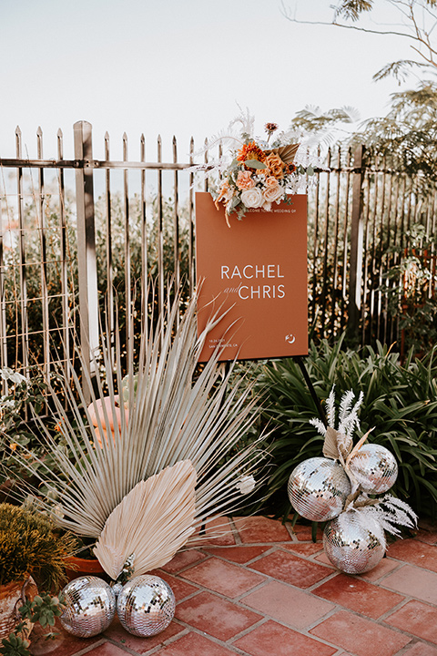  boho beach wedding with Spanish inspired architecture with the bride in a lace gown and the groom in a black tuxedo – ceremony signage 