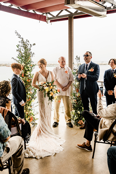  whimsical wedding at an ocean front venue with the groom in a mix and match look with navy and grey colors – couple at ceremony