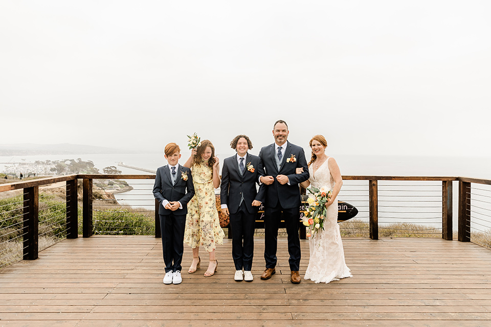  whimsical wedding at an ocean front venue with the groom in a mix and match look with navy and grey colors – couple with family