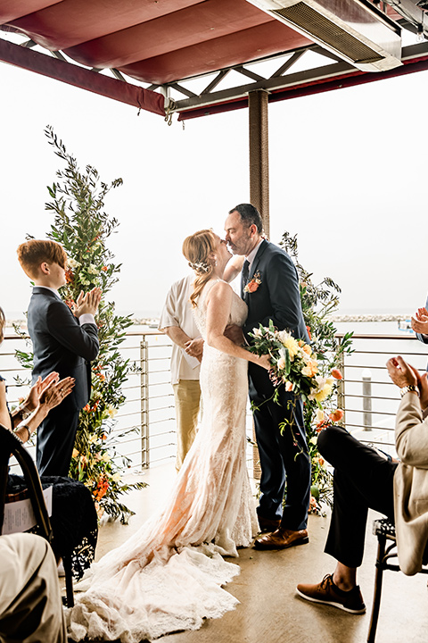  whimsical wedding at an ocean front venue with the groom in a mix and match look with navy and grey colors – couple at ceremony 