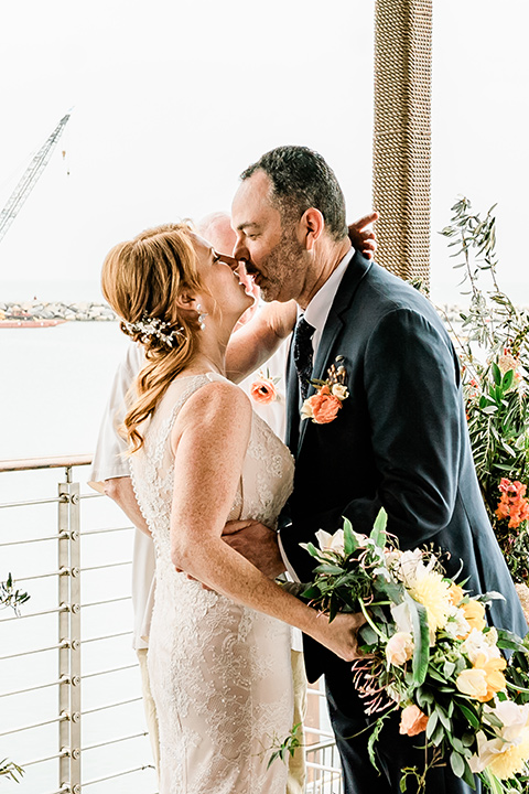  whimsical wedding at an ocean front venue with the groom in a mix and match look with navy and grey colors – couple at ceremony first kisss 