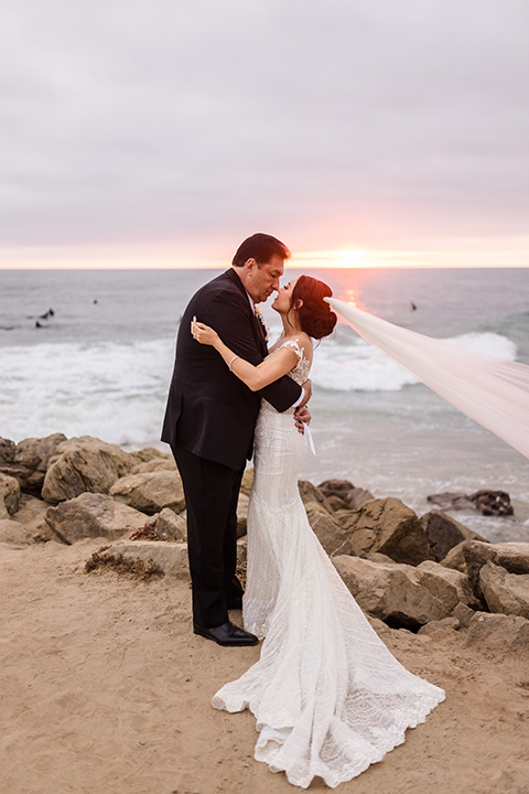  glitz and glam wedding by the beach with the bride in a lace crystal gown and the groom in a black tuxedo – couple on the sand