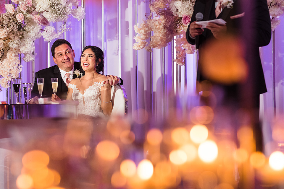  glitz and glam wedding by the beach with the bride in a lace crystal gown and the groom in a black tuxedo – couple sitting at the sweetheart