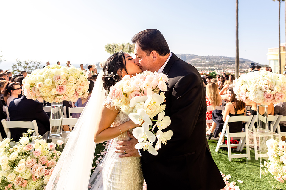  glitz and glam wedding by the beach with the bride in a lace crystal gown and the groom in a black tuxedo – first kiss