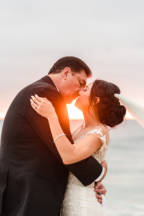  glitz and glam wedding by the beach with the bride in a lace crystal gown and the groom in a black tuxedo – couple on the cliffs