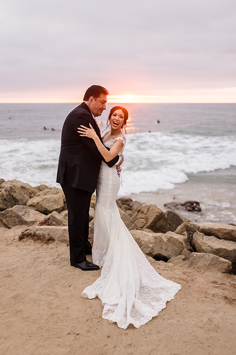 glitz and glam wedding by the beach with the bride in a lace crystal gown and the groom in a black tuxedo – couple on the sand