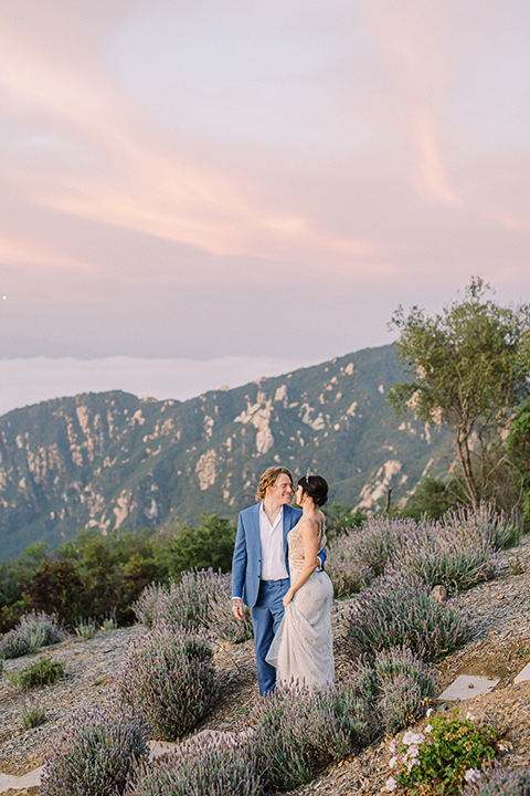  feminine spring editorial at a villa and the groom in a steel blue suit – couple walking on the mountains 