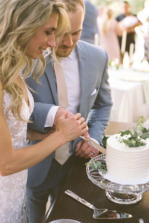  light blue and pink wedding with the groom in a light blue suit and the bride in a lace gown – couple cutting the cake and embracing 