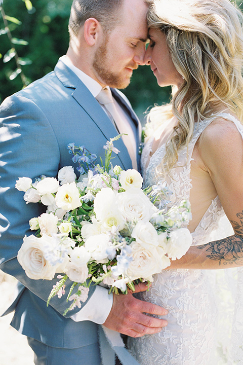  light blue and pink wedding with the groom in a light blue suit and the bride in a lace gown – couple cutting the cake and embracing 