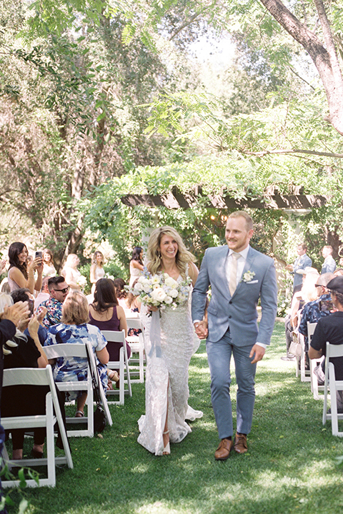  light blue and pink wedding with the groom in a light blue suit and the bride in a lace gown – couple walking down the aisle 