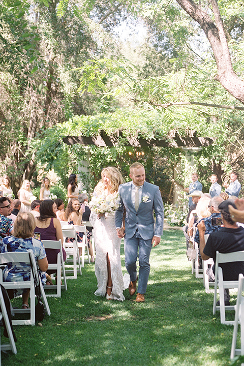  light blue and pink wedding with the groom in a light blue suit and the bride in a lace gown – couple walking down the aisle 