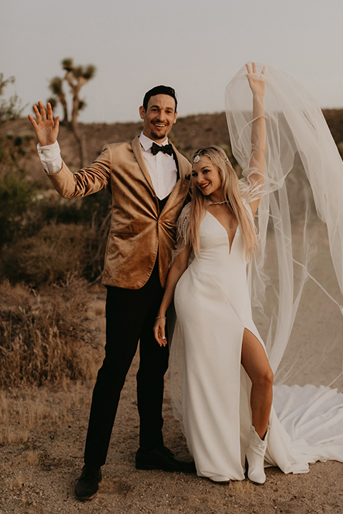  joshua tree wedding with the groom in a gold velvet tuxedo and a black tuxedo and the bride in a flowing gown with bridal wings – couple cheering