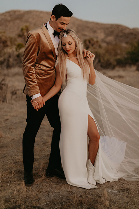  joshua tree wedding with the groom in a gold velvet tuxedo and a black tuxedo and the bride in a flowing gown with bridal wings – couple embracing