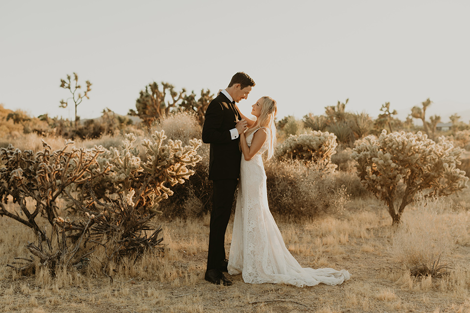  joshua tree wedding with the groom in a gold velvet tuxedo and a black tuxedo and the bride in a flowing gown with bridal wings – couple looking at each other