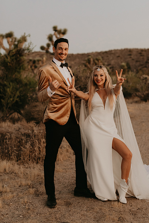  joshua tree wedding with the groom in a gold velvet tuxedo and a black tuxedo and the bride in a flowing gown with bridal wings – couple cheering 