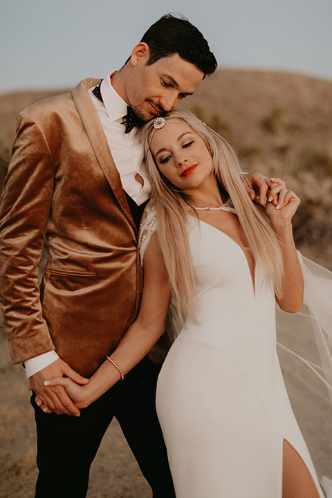  joshua tree wedding with the groom in a gold velvet tuxedo and a black tuxedo and the bride in a flowing gown with bridal wings – couple embracing 