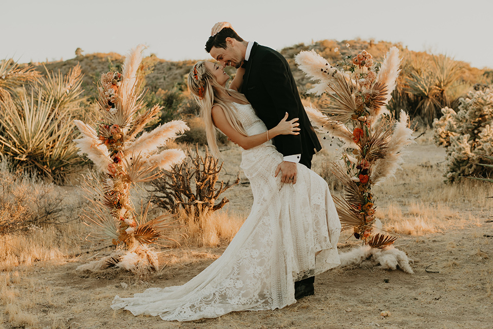  joshua tree wedding with the groom in a gold velvet tuxedo and a black tuxedo and the bride in a flowing gown with bridal wings – first kiss