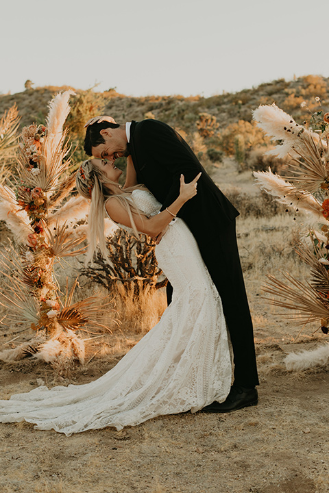  joshua tree wedding with the groom in a gold velvet tuxedo and a black tuxedo and the bride in a flowing gown with bridal wings – first kiss 