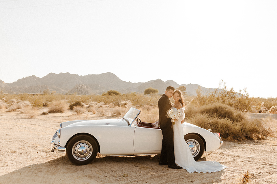  a dessert wedding in Joshua tree shown two ways: a modern black and white theme and a neutral gold and tan theme – groom in a black tuxedo and bride in a modern gown in vintage car