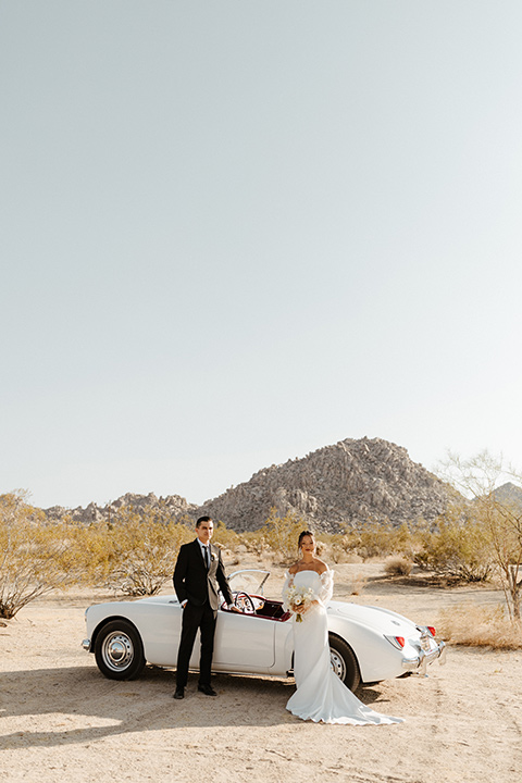  a dessert wedding in Joshua tree shown two ways: a modern black and white theme and a neutral gold and tan theme – groom in a black tuxedo and bride in a modern gown in a vintage car 