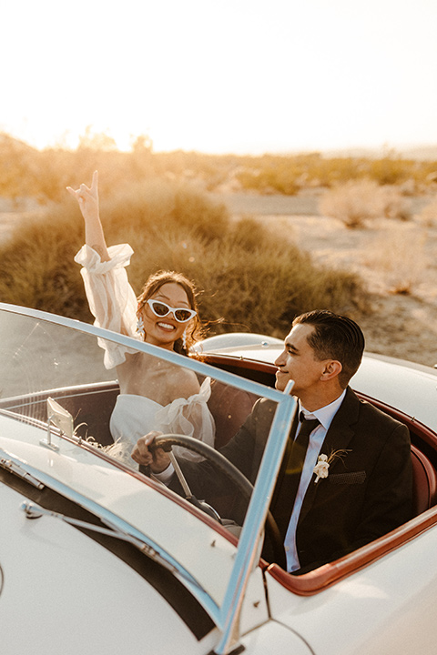  a dessert wedding in Joshua tree shown two ways: a modern black and white theme and a neutral gold and tan theme – groom in a black tuxedo and bride in a modern gown in a vintage car 