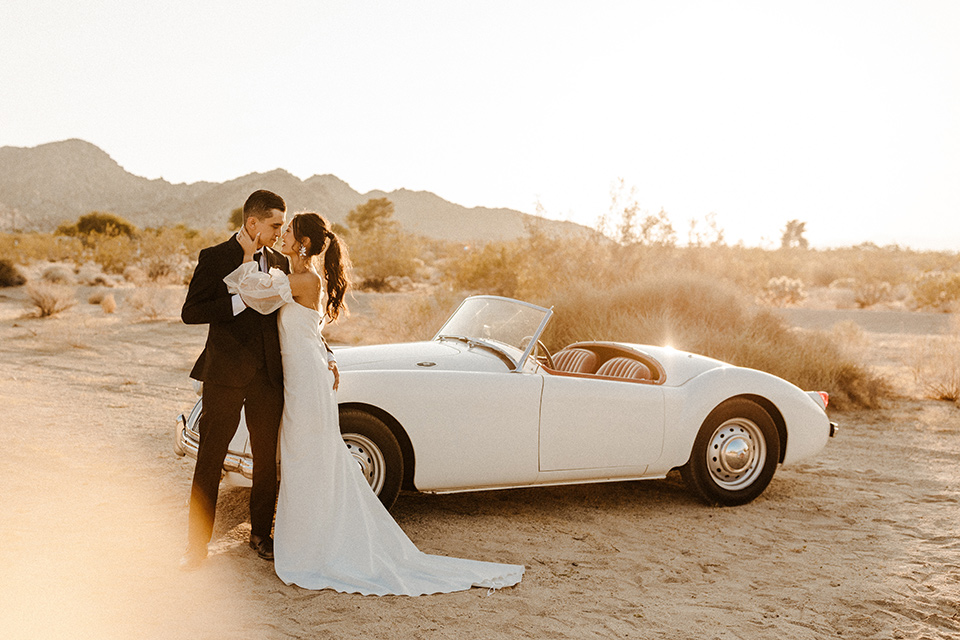  a dessert wedding in Joshua tree shown two ways: a modern black and white theme and a neutral gold and tan theme – groom in a black tuxedo and bride in a modern gown in vintage car