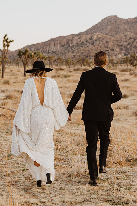  Joshua tree elopement with the bride in a sparkly gown and the groom in a black tuxedo – couple walking away