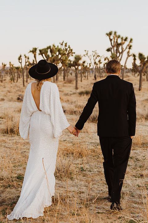  Joshua tree elopement with the bride in a sparkly gown and the groom in a black tuxedo– couple walking away 