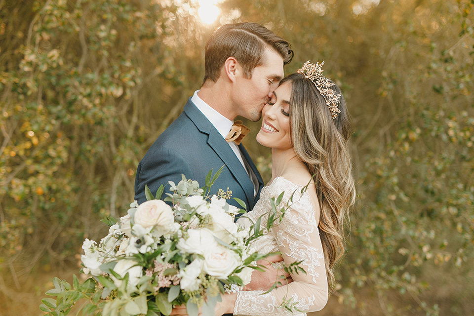  fairytale wedding in the meadow with the bride in a lace long sleeve gown and the groom in a slate blue and café brown look – bride and groom close together 