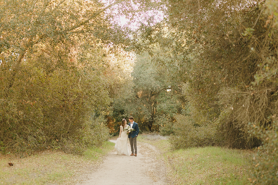  fairytale wedding in the meadow with the bride in a lace long sleeve gown and the groom in a slate blue and café brown look – bride and groom walking 