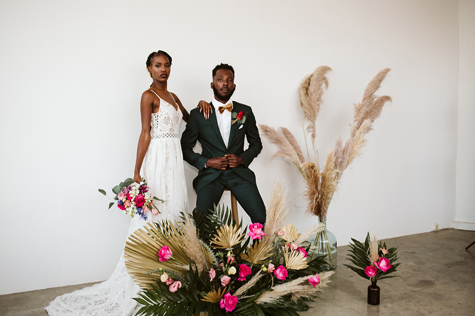  a chic LA studio shoot for a modern boho wedding – with the groom in a white lace gown and the groom in a green suit - bride and groom looking at camera