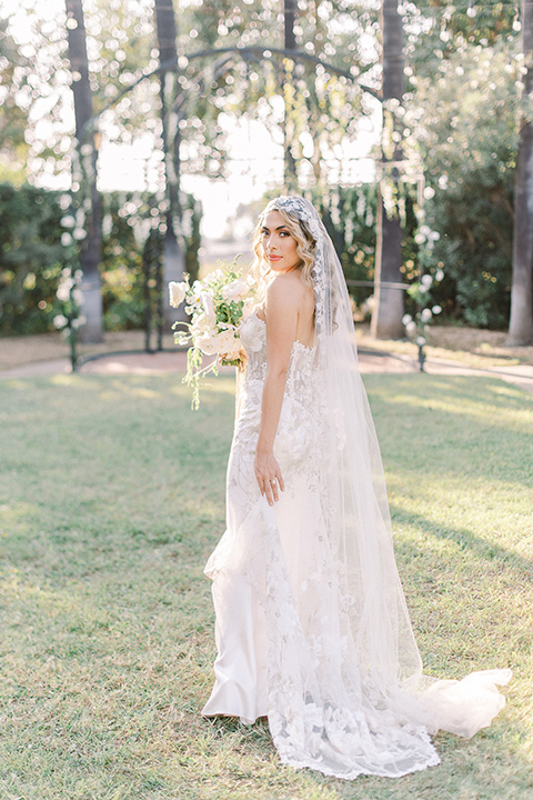  a romantic garden wedding at a Spanish inspired venue with the bride in a lace gown and the groom in a tan suit – bride with her veil on