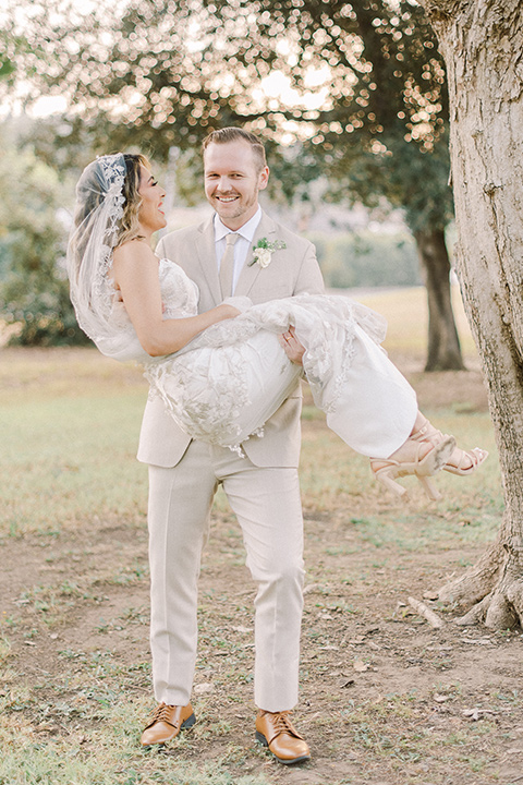  a romantic garden wedding at a Spanish inspired venue with the bride in a lace gown and the groom in a tan suit – groom carrying the bride 