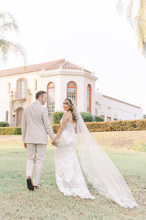  a romantic garden wedding at a Spanish inspired venue with the bride in a lace gown and the groom in a tan suit – couple walking 