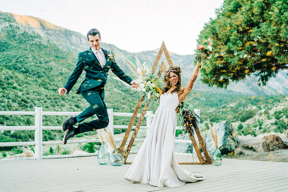  a greenery las vegas wedding at a rustic venue with the bride in an A-line gown and the groom in a green suit – couple jumping